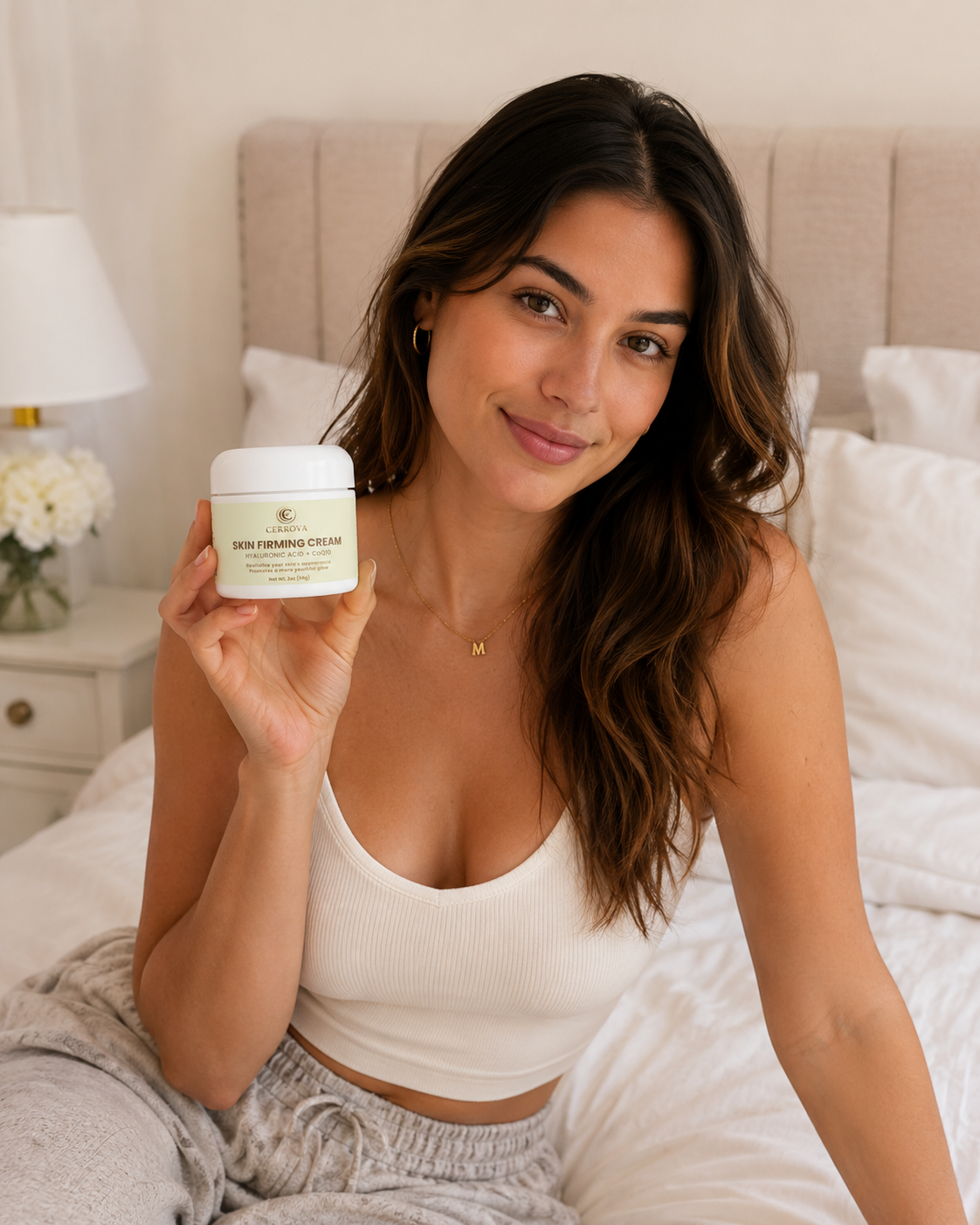 Woman sitting on a bed holding Cerrova Skin Firming Cream with Hyaluronic Acid and CoQ10.